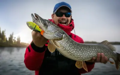 Glücklicher Angler hält stolz einen 1 Meter Hecht, der an einem bunten Köder hängt.