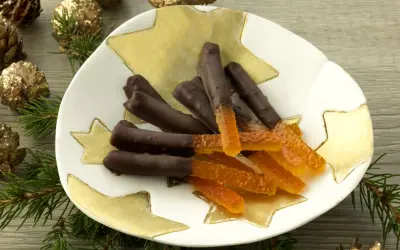 Bâtonnets d'orange confite chocolatés sur une assiette étoilée, entourés de pommes de pin dorées et de branches de sapin.