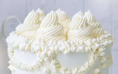 Eine üppige Buttercreme Torte mit kunstvollen Tupfen und Rüschen aus weißer Buttercreme, die auf einem weißen Hintergrund steht.
