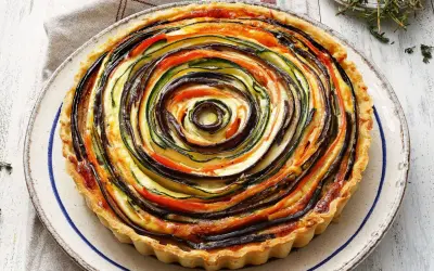 Quiche de verduras con hojaldre, un remolino de calabacín, berenjena y tomate sobre una base dorada.