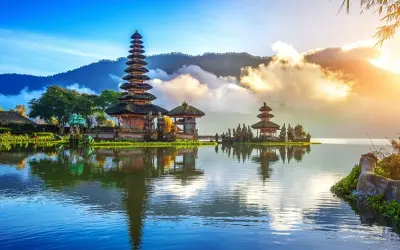 Świątynia Pura Ulun Danu Bratan na Bali, odbijająca się w spokojnej tafli jeziora, otoczona górami i chmurami.