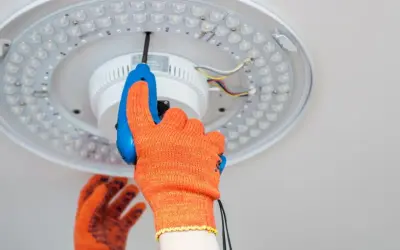 Ręka w pomarańczowej rękawicy przykręca śrubokrętem lampę sufitową LED. Dowiedz się, jak zrobić oświetlenie.