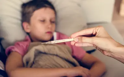 Dziecko 10 lat leży chore, ma zimne ręce. Mama mierzy mu temperaturę.