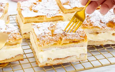 Ein goldener Löffel sticht in ein Stück polnischer Puddingkuchen, bestäubt mit Puderzucker.