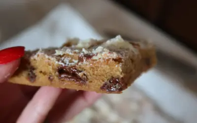 En hand håller en bit av ett blondie recept med chokladbitar.