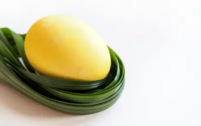 Żółte jajko, pomalowane naturalnym barwnikiem, spoczywa na zielonych liściach.