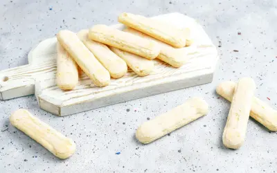Savoiardi pronti per la ricetta del tiramisù, disposti su un tagliere bianco.