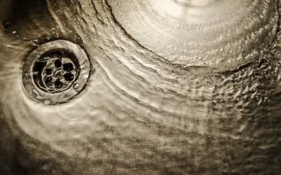 Acqua che scorre su uno scarico metallico, un'immagine che evoca il processo di come sciogliere il grasso nei tubi di scarico.