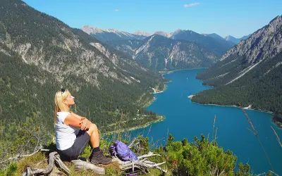 Frau genießt Ausblick beim Plansee Wandern. Türkiser See, grüne Berge und blauer Himmel.