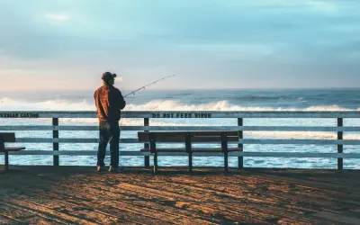 Mężczyzna z wędką na molo, cieszący się spokojnym dniem wędkarza nad wzburzonym oceanem.