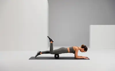 Frau auf einer Matte mit Foam Roller unter dem Oberschenkel, um Hohlkreuz wegtrainieren.