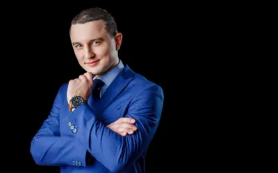 Mężczyzna w niebieskiej marynarce, z rękami skrzyżowanymi na piersi, zastanawia się, jak wkleić zdjęcie do CV.
