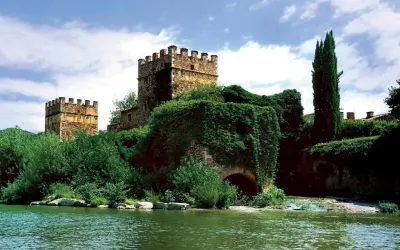 Antiche gualchiere di Remole, torri medievali immerse nel verde, si specchiano in un fiume tranquillo sotto un cielo nuvoloso.