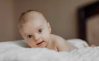Niemowlę z niebieskimi oczami leży na białym kocyku. Jego wzrok jest skupiony, a usta lekko rozchylone. Zez u niemowlaka jest widoczny, ale nie przeszkadza mu w eksplorowaniu świata.