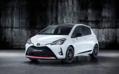 Biały Toyota Yaris GR Sport z czarnym dachem i czerwonymi akcentami, zaparkowany na tle betonowej ściany.