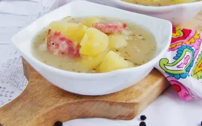 Zalewajka przepis babci: sycąca zupa ziemniaczana z kawałkami wędzonki w białej miseczce na desce.