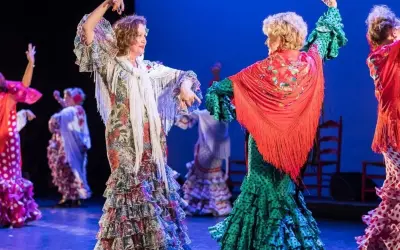 Dos mujeres bailan sevillanas, con volantes y mantones, evocando el origen de esta danza.