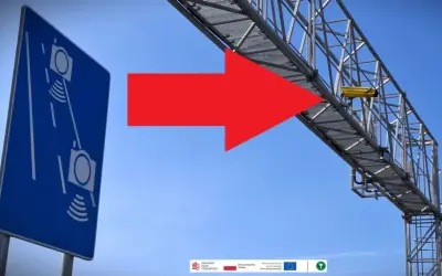 Niebieski znak informuje o odcinkowym pomiarze prędkości S7. Czerwona strzałka wskazuje na żółtą kamerę zamontowaną na konstrukcji nad drogą.