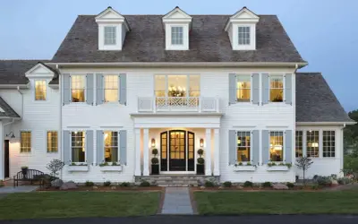 A stately white house with classic colonial architecture, featuring dormer windows, light blue shutters, and a welcoming porch.