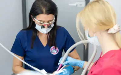 Dentystka z lupami i maską przygotowuje znieczulenie dentystyczne skład. Asystentka trzyma ssak.