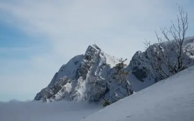 Masyw górski w Tatrach Zachodnich, pokryty śniegiem, z krzyżem na szczycie. W dole morze chmur.