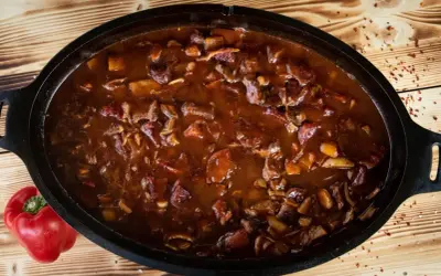 Herzhaftes Gulasch im Dutch Oven, perfekt für rustikale Dutch Oven Rezepte. Daneben liegt eine rote Paprika.