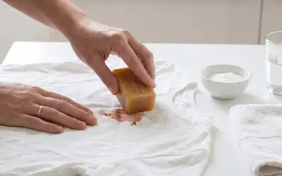 Hand reibt mit Kernseife über Blutfleck auf weißem T-Shirt. So lässt sich blut aus kleidung entfernen.