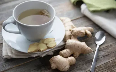 Kubek z herbatą imbirową, plasterki imbiru i korzenie. Czy imbir można pić codziennie? Odpowiedź może być w tym naparze.