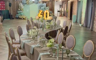 Eleganckie przyjęcie weselne na 40 osób. Stoły nakryte, ozdobione kwiatami i świecami. W tle dekoracje z balonów i podświetlana liczba 40.