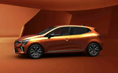 Pomarańczowy Renault Clio 6 z nowoczesnym designem, prezentowany na tle architektonicznych form w odcieniach brązu.