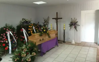 Drewniana trumna otoczona wieńcami i kwiatami, krzyż i świece tworzą najpiękniejsze ostatnie pożegnanie.