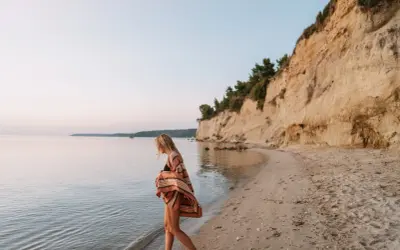 Mujer rubia camina por la playa, sintiendo la brisa marina. Ella anhela la libertad y el deseo de querer viajar sola.