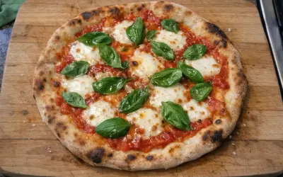 En nybakad pizza med tomatsås, smält mozzarella och färsk basilika på en träskärbräda.
