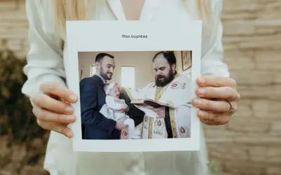 Carte "Mon baptême" tenue par des mains. Photo d'un bébé pleurant, tenu par son père, recevant le baptême d'un prêtre. Un beau texte baptême pour les grands-parents.