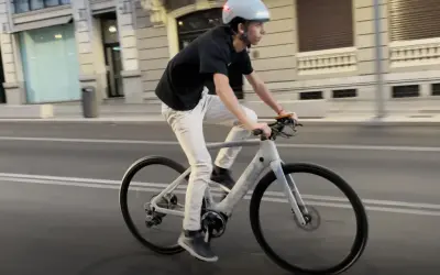 Un joven con casco y ropa casual pedalea una bicicleta eléctrica por la ciudad.
