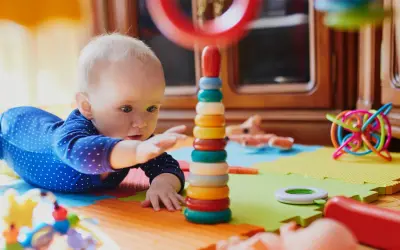 Zaintrygowany 6 miesięczne dziecko sięga do kolorowej wieży z kółek, otoczony zabawkami na macie.