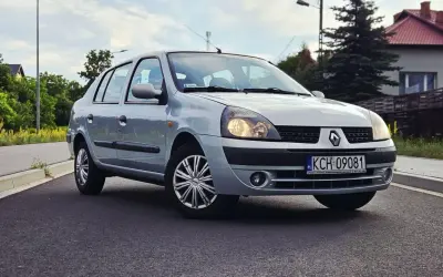 Srebrny Renault Thalia 1.4 z polskimi tablicami rejestracyjnymi KCH 09081 zaparkowany na poboczu drogi.