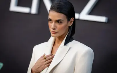 Laysla de Oliveira, elegant in a white blazer, poses with a hand on her chest, adorned with a striking gold ring.