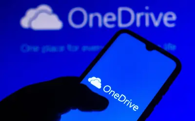Dłoń trzyma smartfon z ikoną OneDrive. Szybki OneDrive download ułatwia dostęp do plików.
