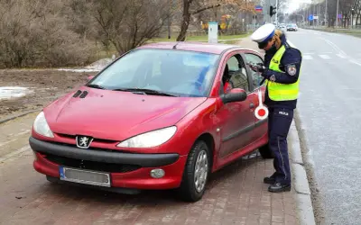 Policjantka w kamizelce odblaskowej i czapce spisuje kierowcę przy czerwonym samochodzie.