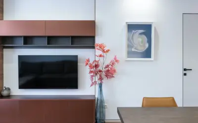 En modern inredning med en stor TV och flera tavlor runt om. En vas med röda höstblad står bredvid.
