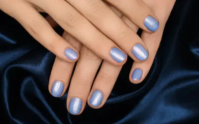 Mani curate con unghie corte rotonde smaltate di un azzurro perlato, adagiate su un tessuto blu notte.