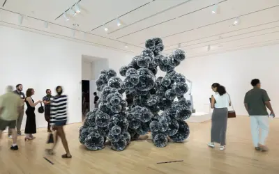 Visitors admire a large, dark, spherical sculpture in a bright gallery space, typical of Indianapolis Museum of Art photos.