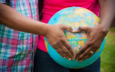 Mani a forma di cuore circondano un globo, simbolo del desiderio di adottare un bambino e accoglierlo nel mondo.