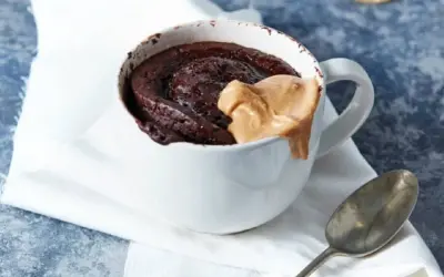 Schokoladiger high protein tassenkuchen mit Erdnussbutter-Topping in einer weißen Tasse, daneben ein Löffel.