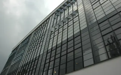 Fasada budynku w stylu modernizm, z rzędem przeszklonych okien i charakterystycznymi, wychylonymi świetlikami.