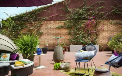 Acogedor **diseño terraza exterior** con muebles de ratán, sillas azules, plantas exuberantes y detalles decorativos en ladrillo.