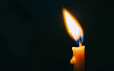 Płonąca świeca w ciemności, symbol pamięci i wzruszające cytaty na rocznicę śmierci.