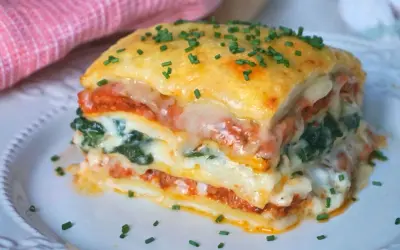 Porción de lasaña de espinacas, con capas de pasta, salsa de tomate, queso derretido y espinacas, espolvoreada con cebollín.
