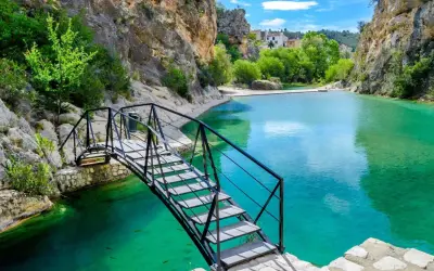 Puente metálico sobre aguas turquesas en uno de los lagos en Valencia, rodeado de rocas y vegetación.